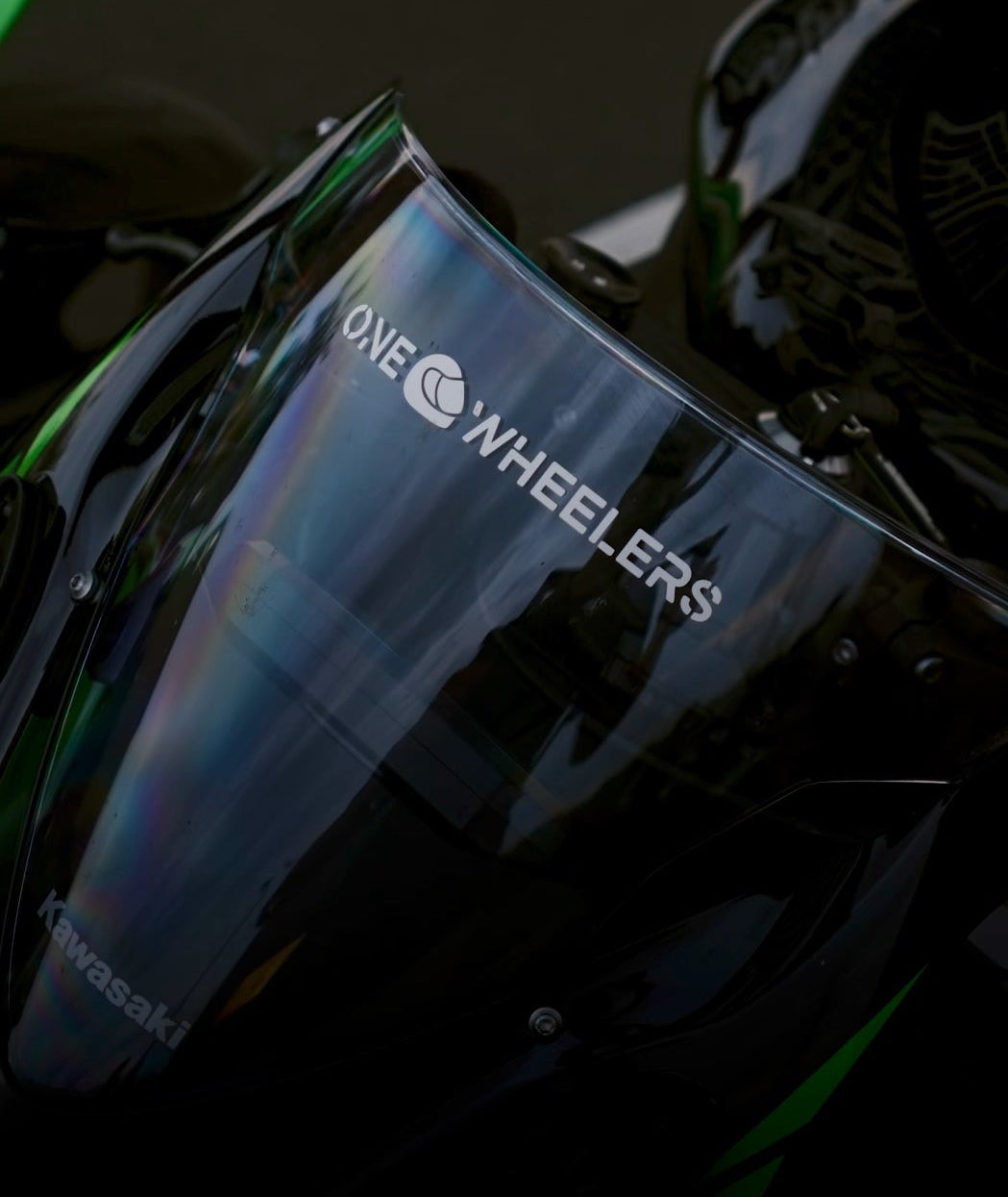 Motorcycle windshield with 'One Wheelers' branding on a dark background